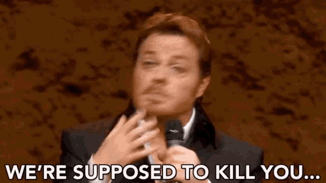 a man is holding a microphone in his hand and saying `` we 're supposed to kill you ... ''