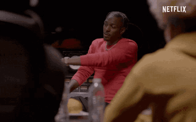 a man in a red sweater is sitting at a table with a bottle of water in front of him and a netflix logo