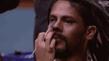 a man with dreadlocks and a beard is getting his makeup done by a woman .