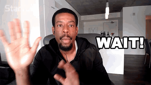 a man with a beard and ear buds says " wait "