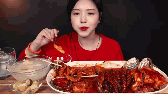 a woman in a red shirt is eating a large plate of food with chopsticks