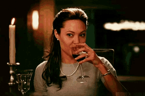 a woman is sitting at a table drinking a glass of red wine .