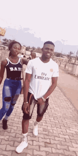 a man in a fly emirates shirt stands next to a woman