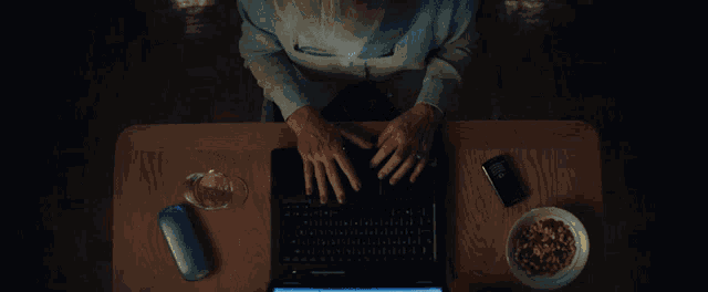 a person is typing on a laptop with a phone and a bowl of cereal