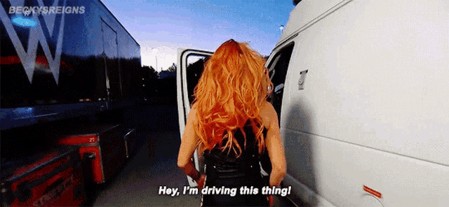 a woman with red hair is standing next to a white van and says hey i 'm driving this thing !
