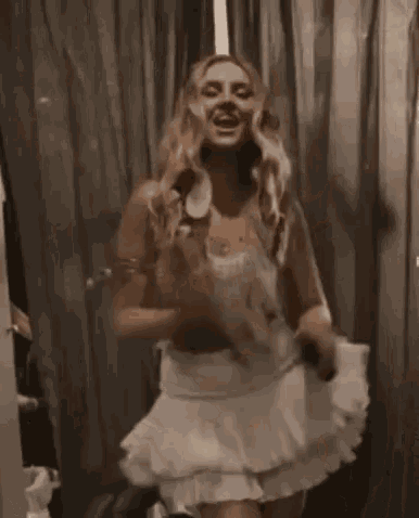 a woman in a white dress is standing in front of a window and laughing .