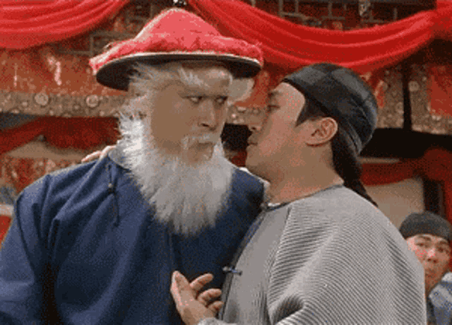 a man with a white beard and a red hat is talking to another man