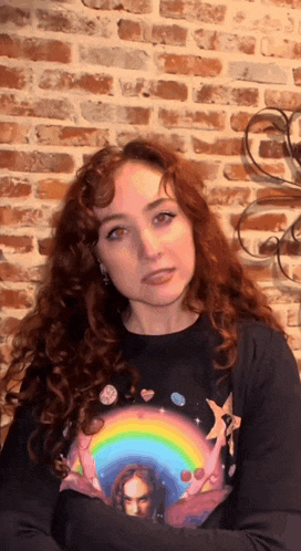a woman with red hair is wearing a black shirt with a rainbow and jesus on it