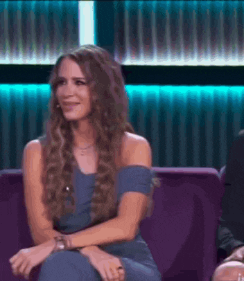a woman with long hair is sitting on a purple couch and smiling .