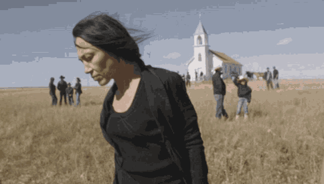 a woman stands in a field in front of a small white church