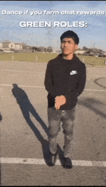 a man in a black hoodie is standing in a parking lot with a shadow on the ground .