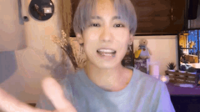 a young man with gray hair is smiling and waving at the camera while wearing a blue shirt .