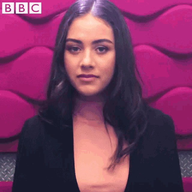 a woman is sitting in front of a pink wall and making a funny face .