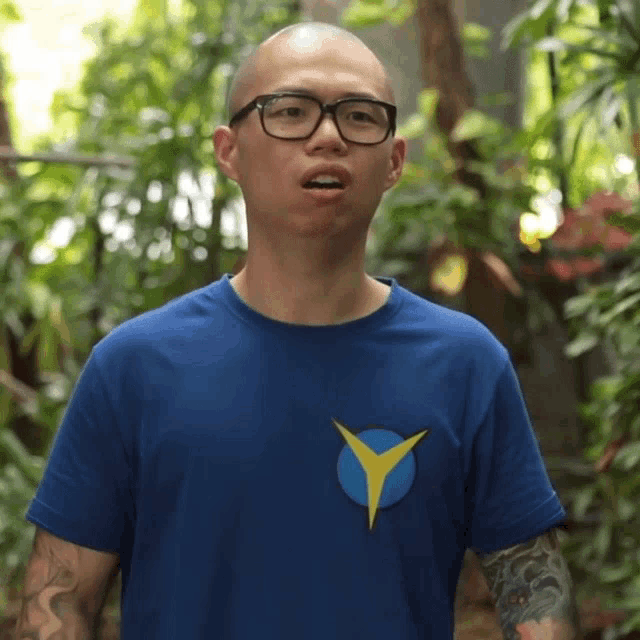 a man wearing glasses and a blue shirt has a yellow y on his chest
