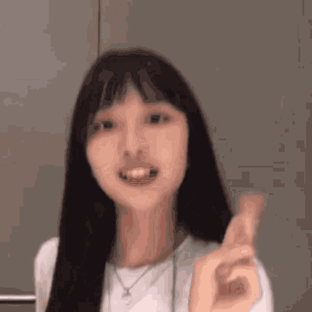 a woman with long black hair and a white shirt is making a funny face .