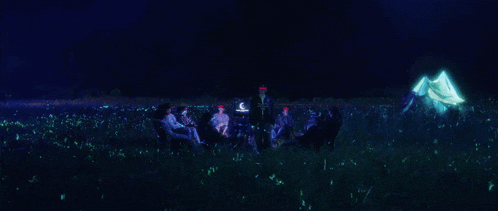 a group of people are sitting in a field with glowing flowers