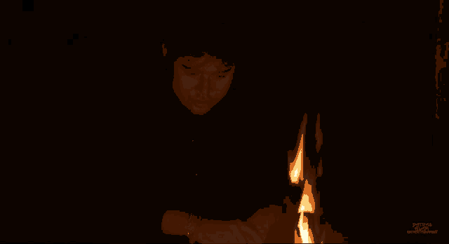 a man in a black shirt stands in front of a fire in a dark room