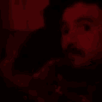 a man with a beard is smoking a cigarette in a dark room in a blurry photo .
