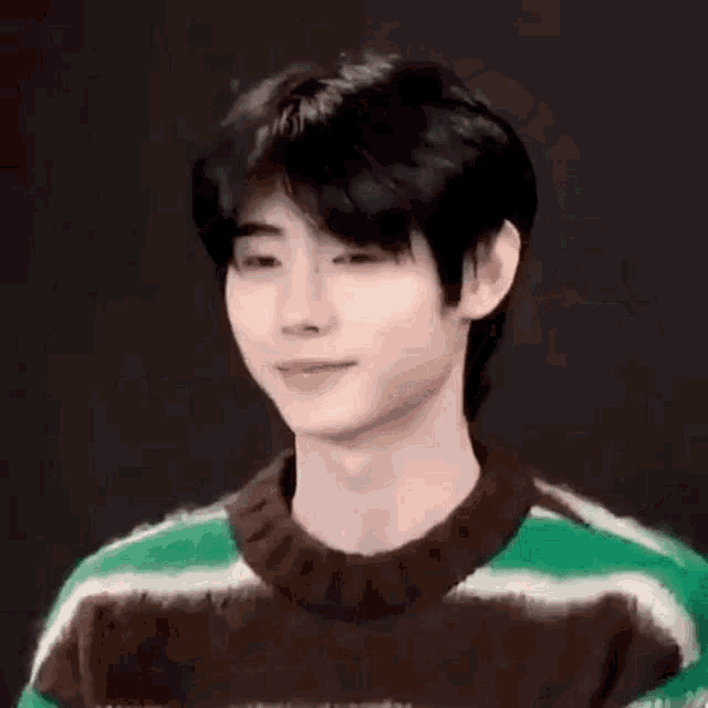 a young man wearing a green and brown striped sweater is covering his ears .