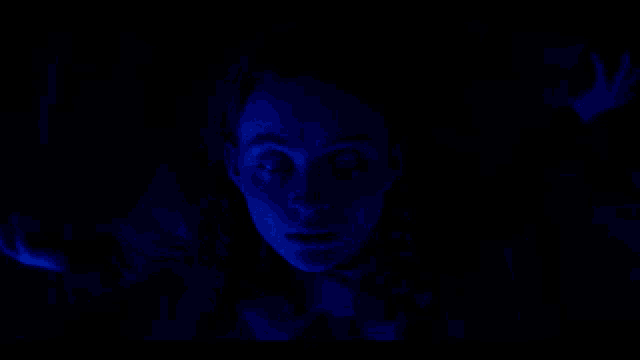 a woman 's face is glowing in a dark blue light