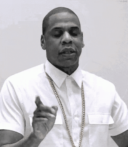 a man wearing a white shirt and a gold chain is pointing at something .
