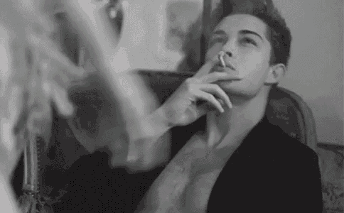 a man is smoking a cigarette while sitting in a chair .