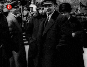 a man in a hat stands in front of a crowd with the letter h on the bottom left