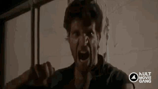 a man is screaming in front of a wall with the kult movie gang logo in the corner