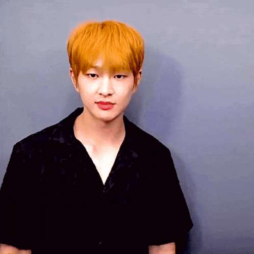 a young man with orange hair and a black shirt looks at the camera