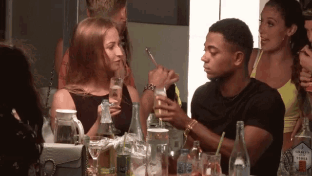 a group of people are gathered around a table with a bottle of gold 's vodka