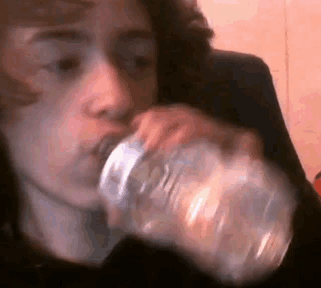 a young man is drinking water from a clear plastic bottle .