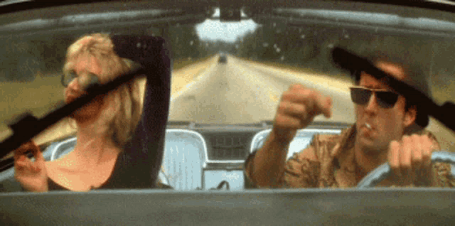 a man and a woman are sitting in a car and the woman is adjusting her windshield wiper