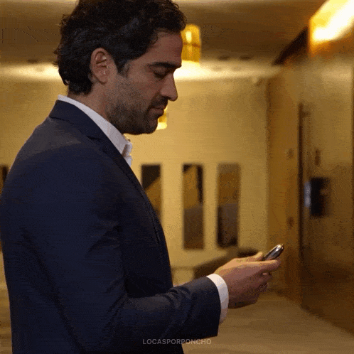 a man in a suit is looking at his cell phone with lucasporroncho written in the corner
