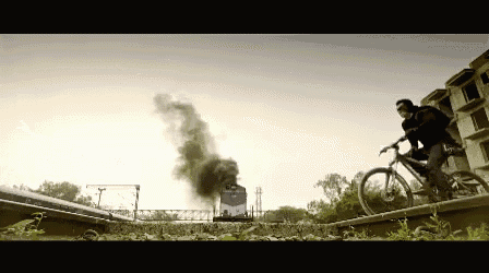a man riding a bike on train tracks with smoke coming from a train in the background