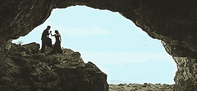 a man and a woman standing in a cave looking out
