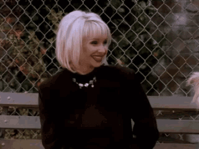 a woman with blonde hair is sitting on a bench with a dog .