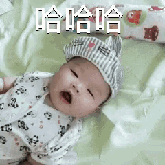 a baby wearing a striped hat is laying on a bed with its mouth open .