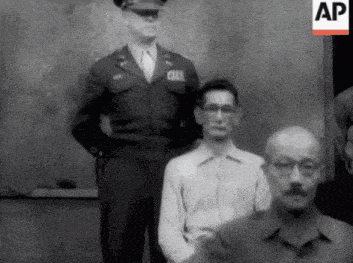 a man in a military uniform stands next to a man in a white shirt with glasses