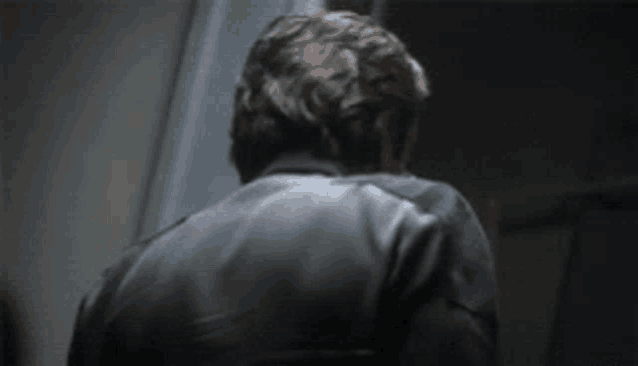 a man in a black jacket is standing in a dark room and looking at the camera .