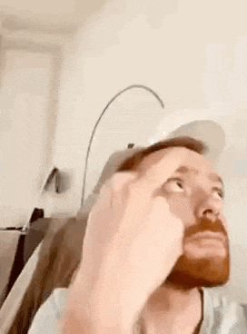 a man with a beard is wearing a hat and giving the middle finger .