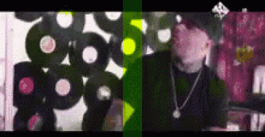 a man with a necklace is standing in front of a wall of vinyl records .
