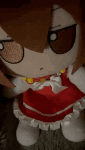 a stuffed doll with brown hair and a red dress is sitting on a carpet .