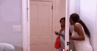two women are standing in a doorway talking to each other . one of the women is holding a cell phone .