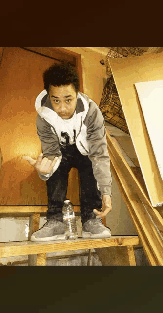 a young man standing on a wooden ladder with a bottle of aquafina water