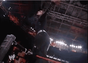 a wrestler is flying through the air with his arms outstretched in a dark room