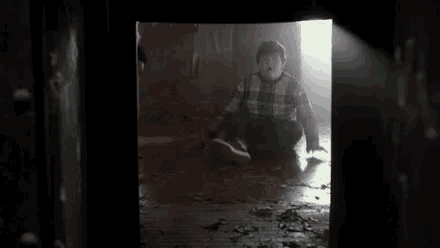 a boy is sitting on the floor in a dark room with a light coming through the door .