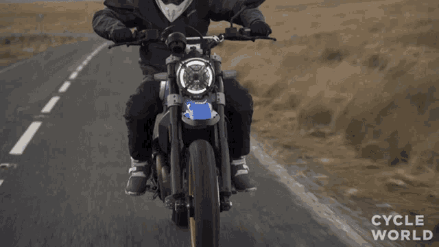 a man riding a motorcycle on a road with the words cycle world written on the bottom