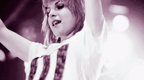 a woman in a white shirt is standing on a stage with her arms outstretched .