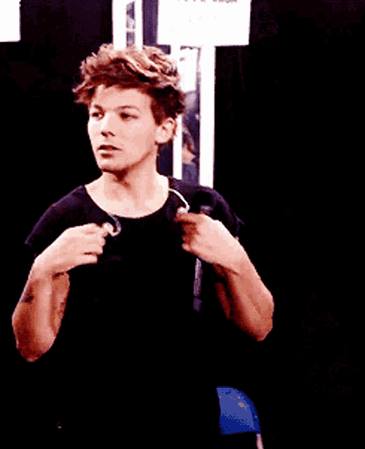 a young man in a black shirt stands in front of a sign that says one direction