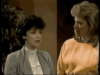 two women are standing next to each other and one is wearing a yellow sweater .